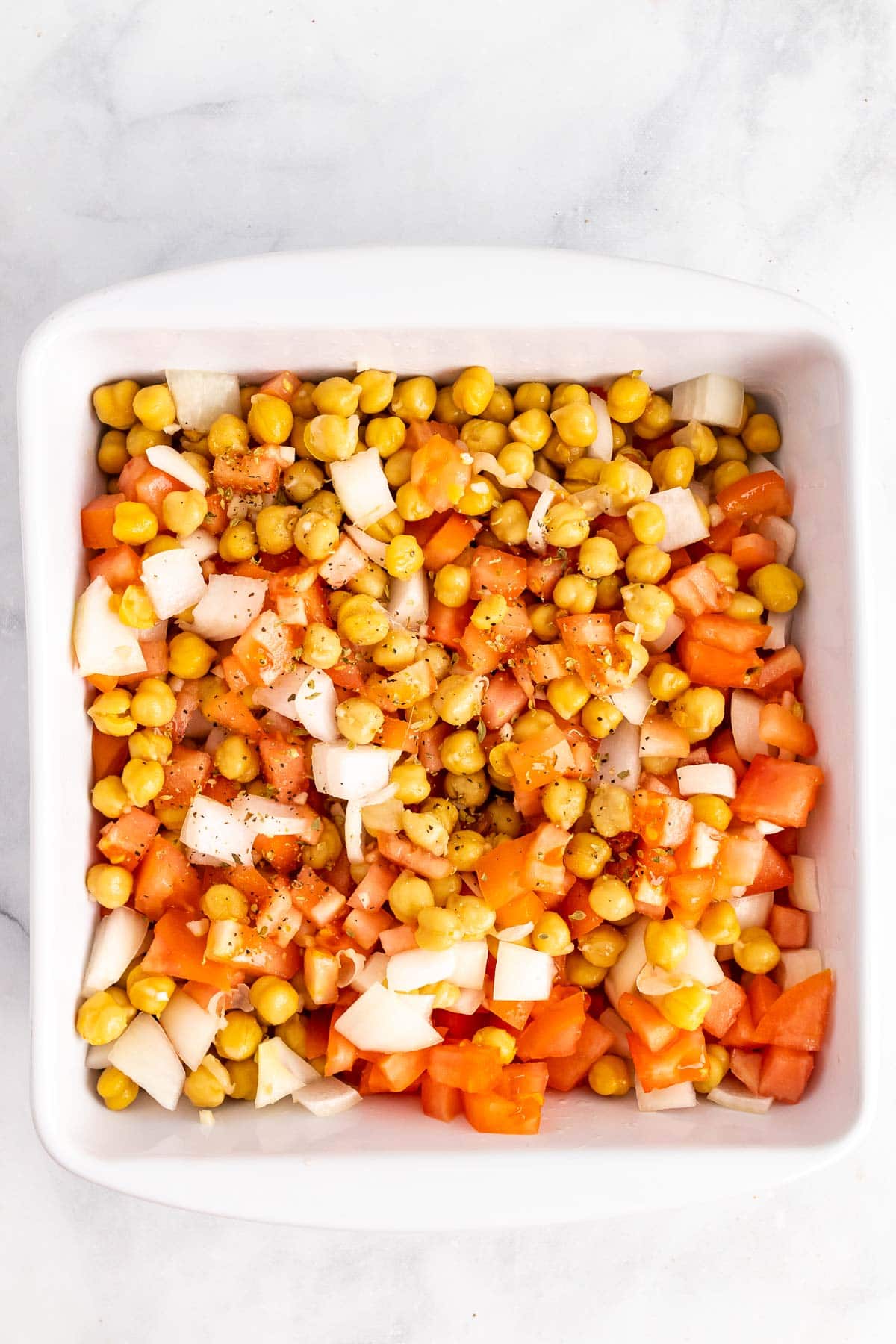 Chickpeas, onion, and tomato sprinkled with spices in a baking dish