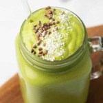 Green smoothie in a glass jar with a straw topped with seeds and coconut