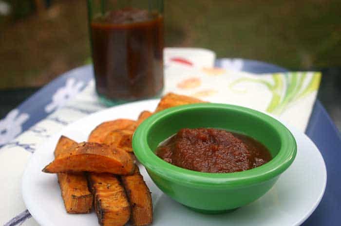 Quick and Easy Homemade Ketchup in a green ramekin on a white plate next to sweet potato fries