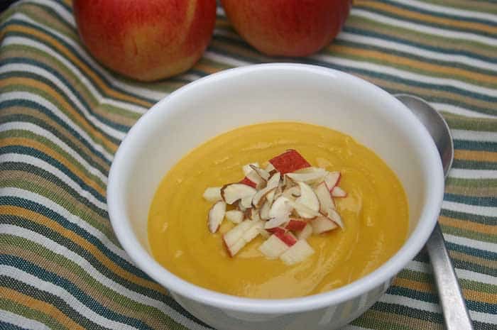 Spicy Apple Squash Soup in a white bowl on a striped placemat, topped with diced apple and almond slivers