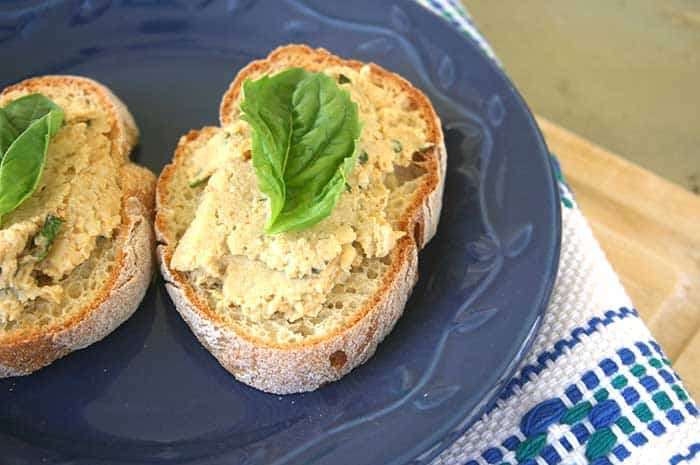 Artichoke Hummus spread onto baguette slices and garnished with basil