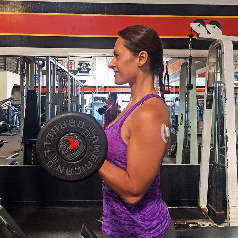 Christel doing biceps curls in the gym with a Dexcom CGM on her upper arm