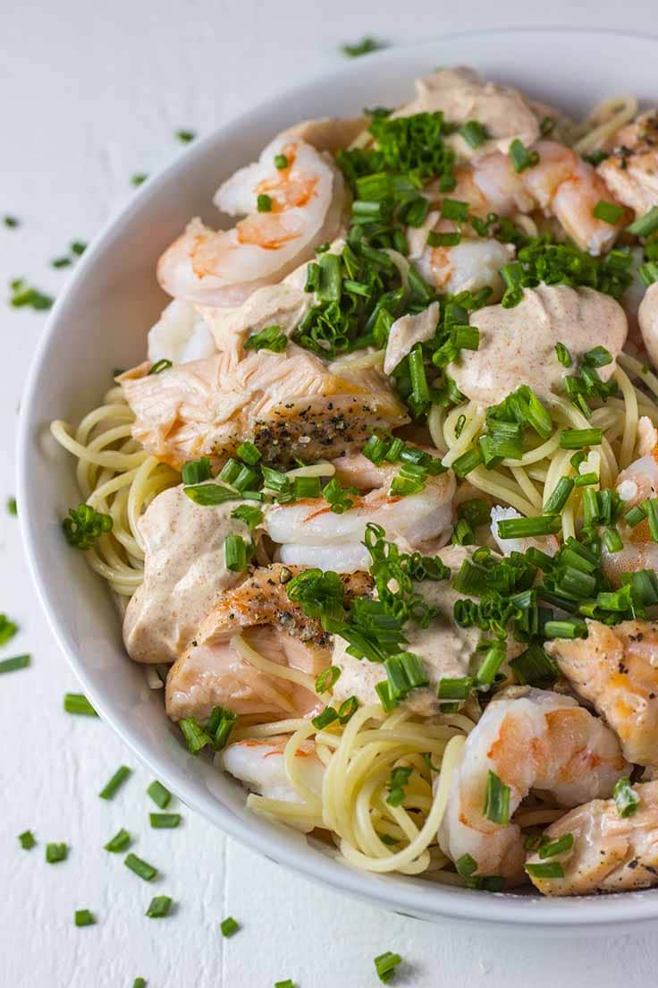Salmon & Shrimp pasta in a bowl over whole wheat pasta with chives on top