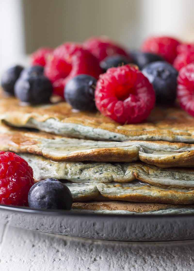 A stack of Protein Pancakes on a black plate with mixed berries on top.