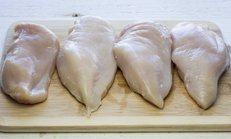 Four cleaned chicken breasts on a cutting board