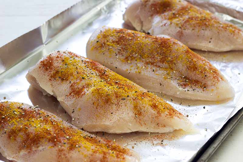 Four seasoned chicken breast on a baking sheet lined with aluminum foil