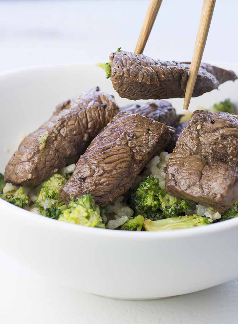 Marinated steak and broccoli in a bowl over cooked rice
