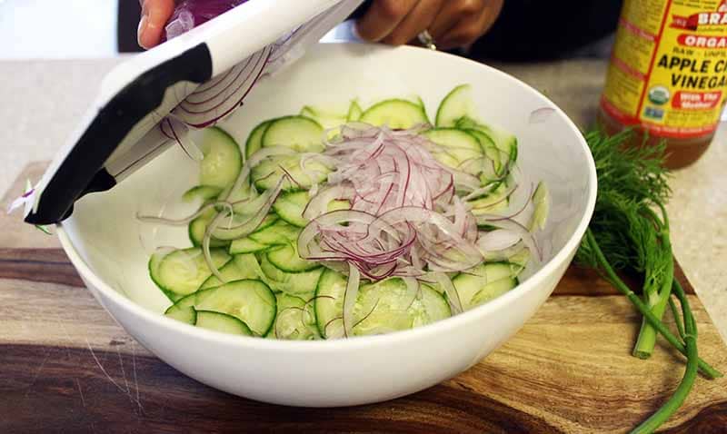 Thin-sliced cucumber and onion in a bowl with chopped dill.