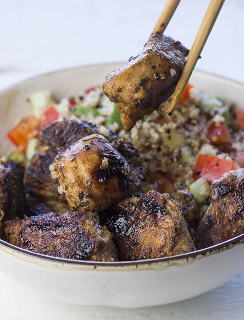 Chopsticks holding a piece turkey over a bowl of quinoa