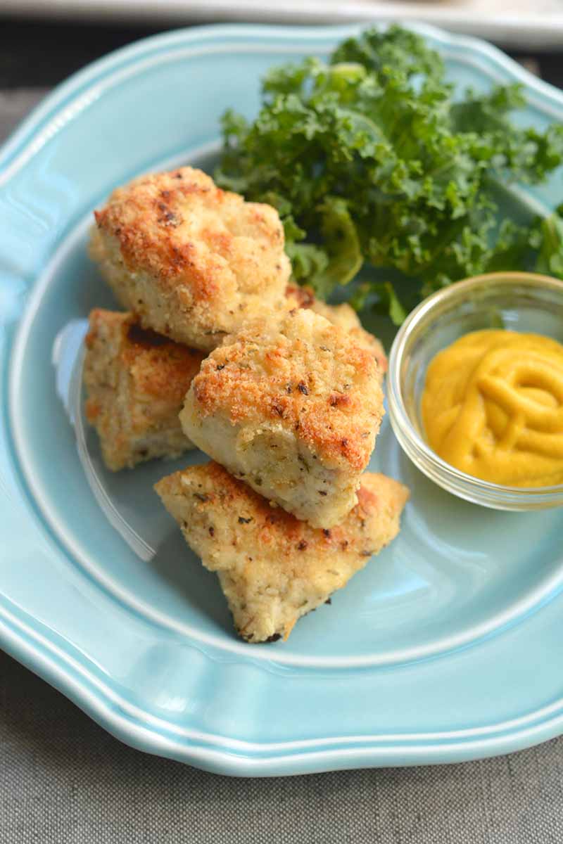 Homemade chicken nuggets on a blue plate with salad and mustard dressing