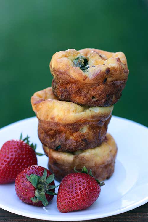 Stack of three mini frittatas on a white plate next to strawberries