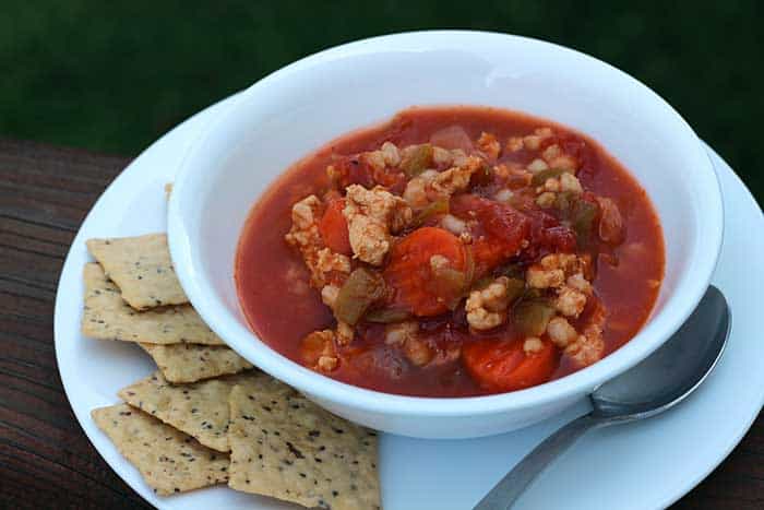 Turkey Barley Vegetable Soup in a white bowl on a white plate with a few crackers and a spoon