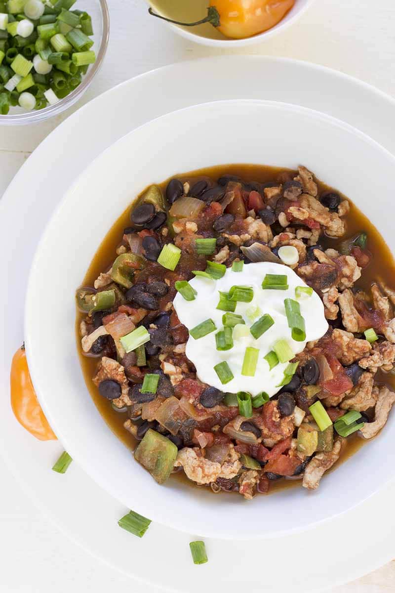 A bowl of turkey chili, topped with sour cream and sliced green onion, as seen from above