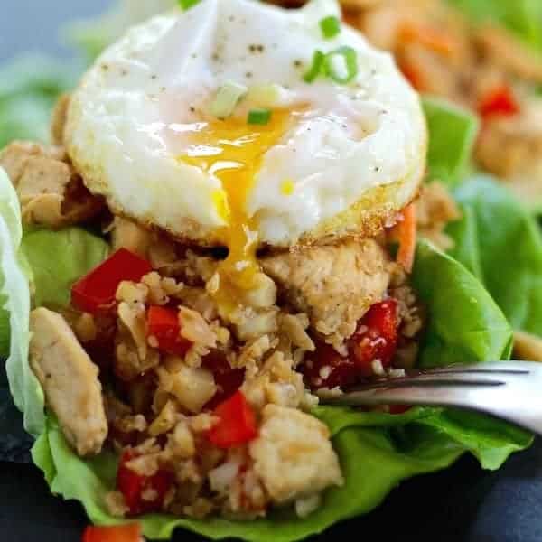 Fried egg on top of the lettuce wraps with yolk running into the chicken filling