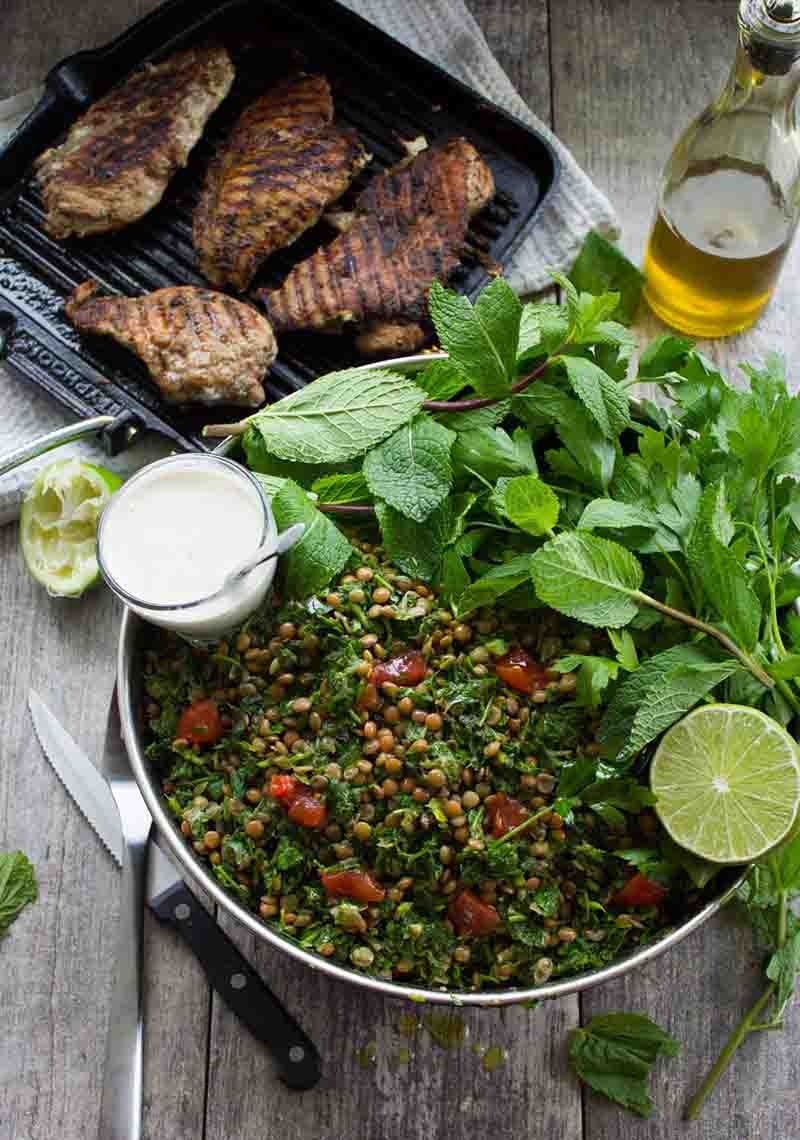 Tabbouleh with lentils, served with tahini sauce, mint leaves, and a lime in the bowl and grilled chicken on the side