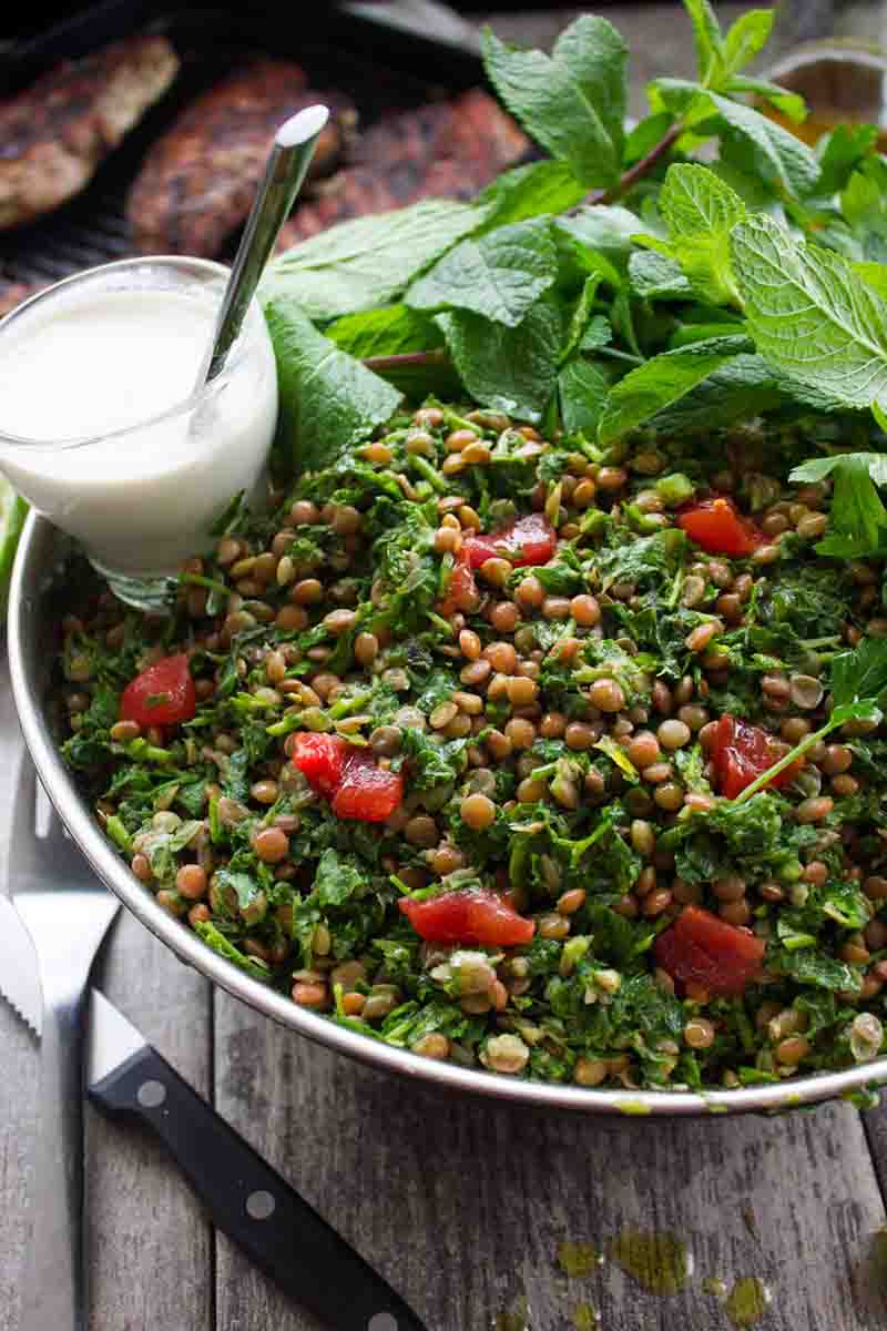 Lentil tabbouleh with grilled chicken in a large bowl with a side of tahini sauce and mint leaves