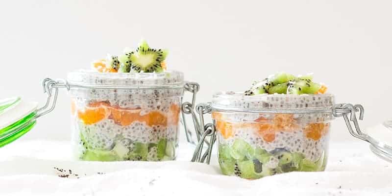 2 mason jars with coconut chia pudding, fruit, and shredded coconut.