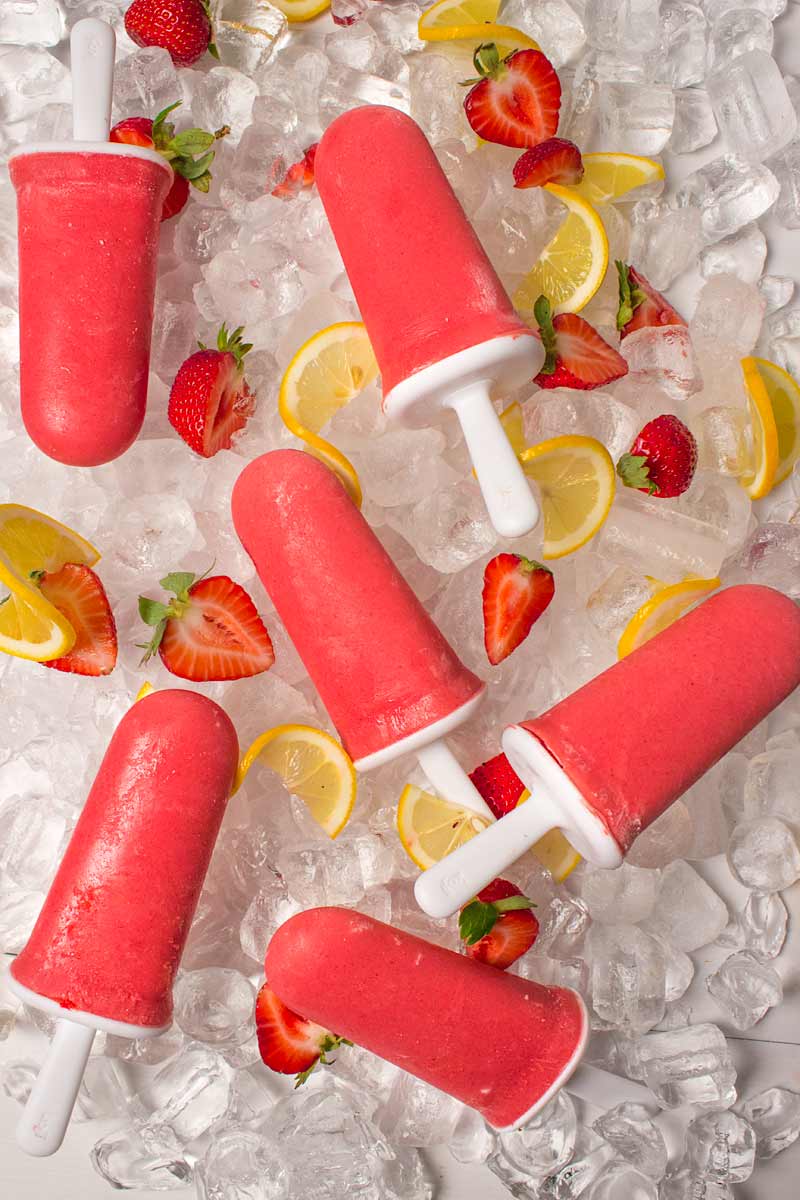 Sugar Free Strawberry Lemonade Popsicles on a bed of ice cubes and strawberries