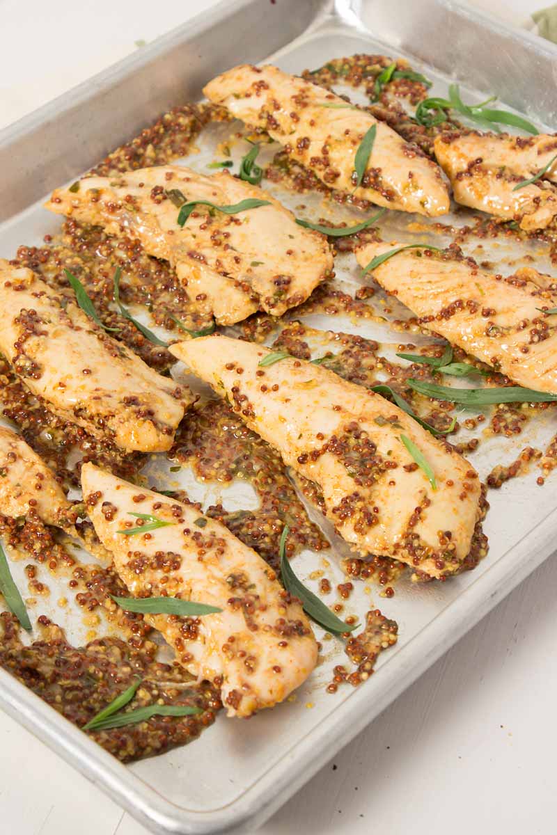 Cooked chicken tenders laid out on a baking dish with mustard sauce over them