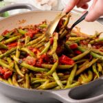 Thongs lifting some Green Beans with Stewed Tomatoes from a pan