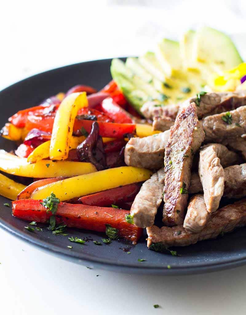 Meat, peppers, and sliced avocado separated on a plate for these easy beef fajitas