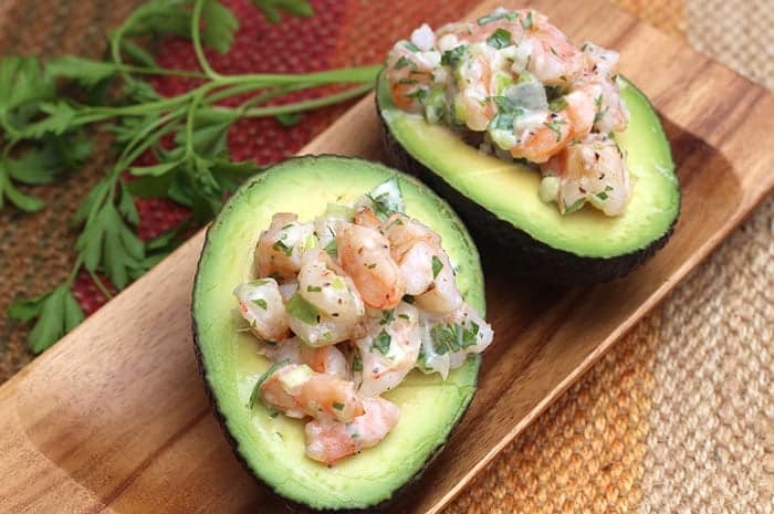 Two Shrimp Salad Stuffed Avocado halves on a cutting board with parsley in the background