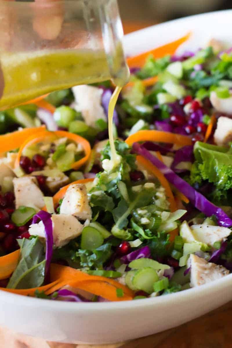 Pouring vinaigrette on top of the salad in a bowl.