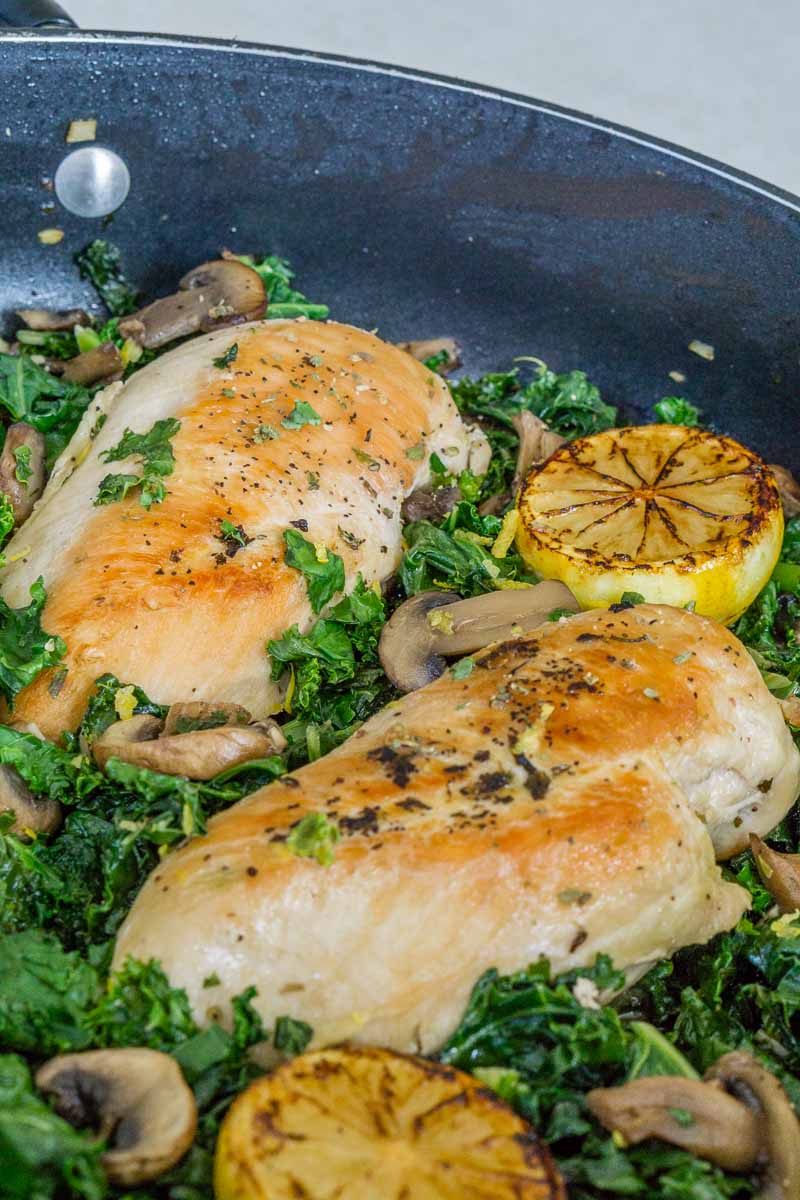 Chicken breasts, mushrooms, and kale cooking in the pan