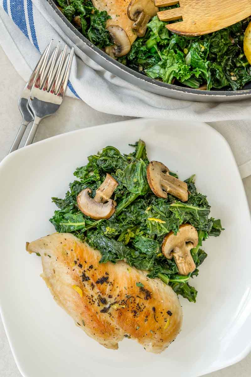 Chicken, kale, and mushrooms plated on the table next to the pan