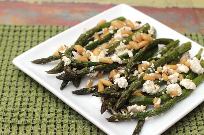 Roasted Asparagus with Goat Cheese and Pine Nuts on a white plate on top of a cloth napkin