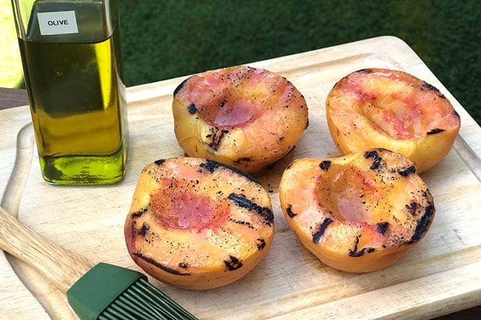 2-Ingredient Grilled Peaches on a cutting board next to olive oil and a grill brush