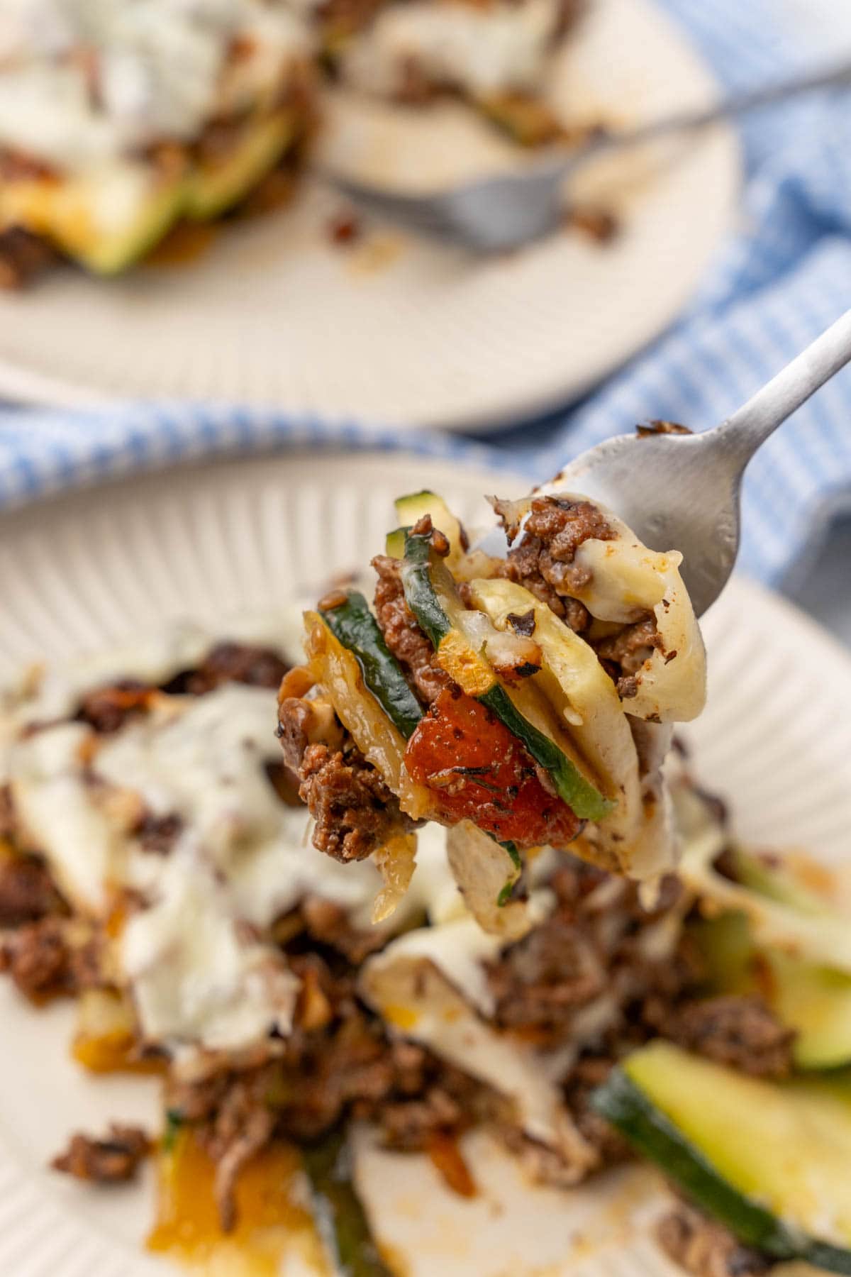 Fork holding a bite of zucchini lasagna over a plate of lasagna