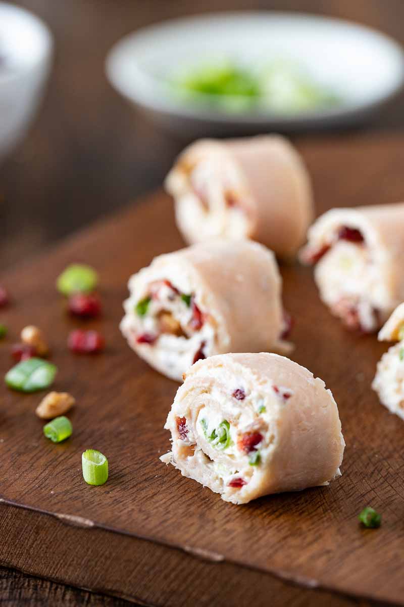 Sliced turkey rolls on a cutting board with green onions and cranberries