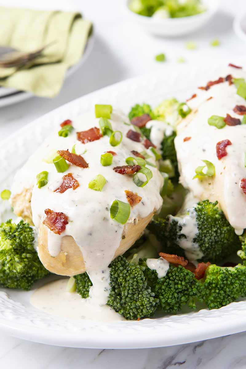 Crockpot ranch chicken garnished with bacon and green onion over broccoli