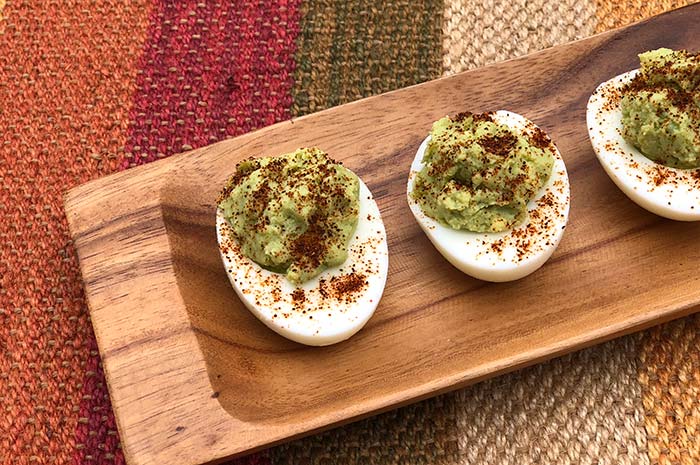 3-Ingredient Guacamole Deviled Eggs seasoned with chili powder on a wood serving tray
