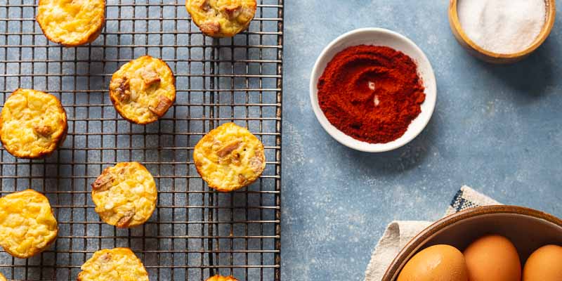 Mini quiches on a cooling rack next to a ramekin of paprika
