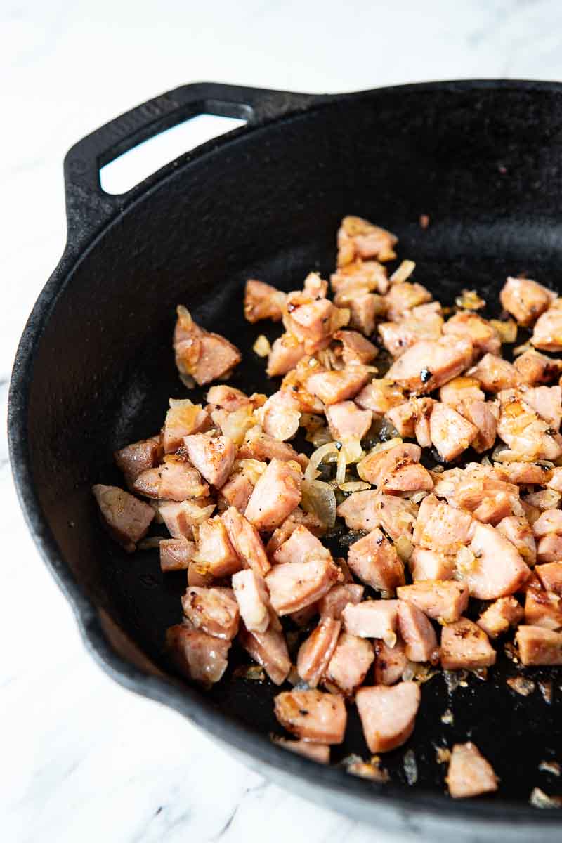 sausage and onions cooking in a cast iron pan