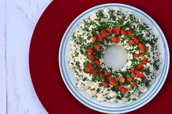 Holiday Cheese Ball Wreath on a white plate topped with chopped peppers and fresh chopped herbs, as seen from above.
