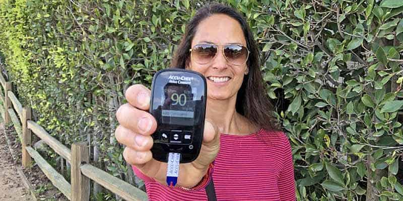 Christel holding a blood glucose monitor showing a 90 mg/dl blood sugar level