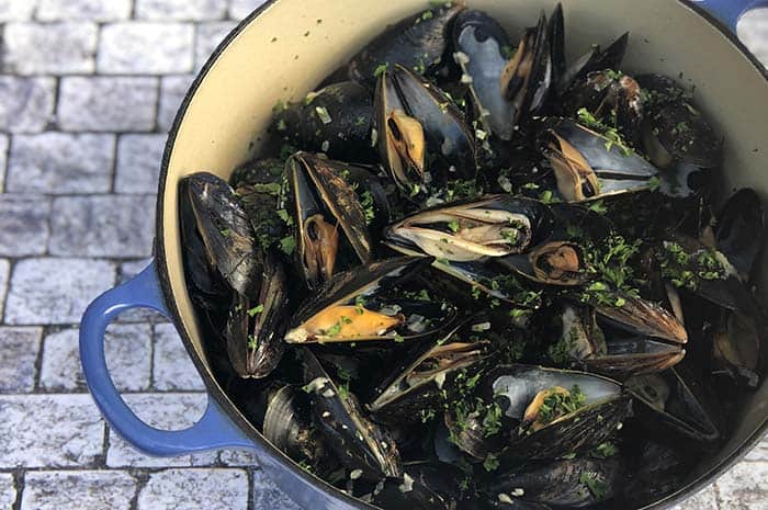 Mussels in White Wine Sauce (Moules Marinière) in a blue pot on cobblestone