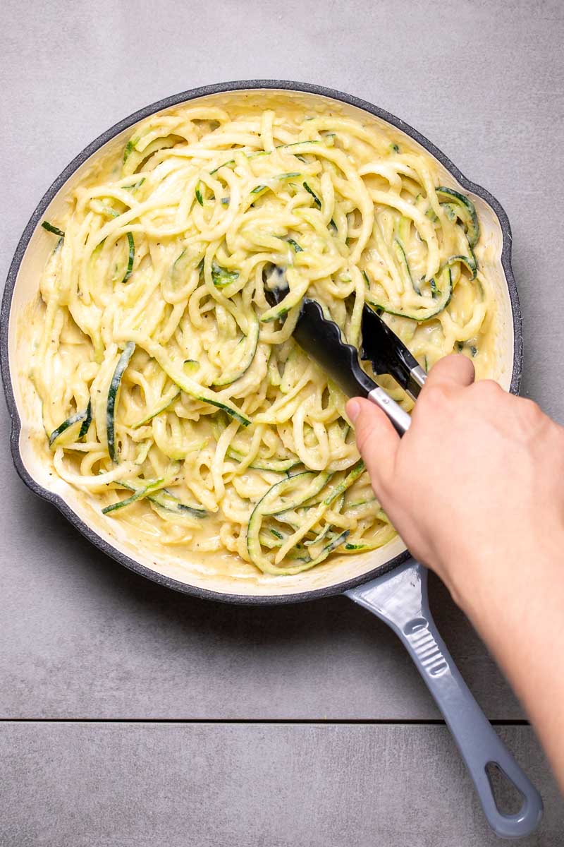 Alfredo sauce and zucchini noodles being mixed together