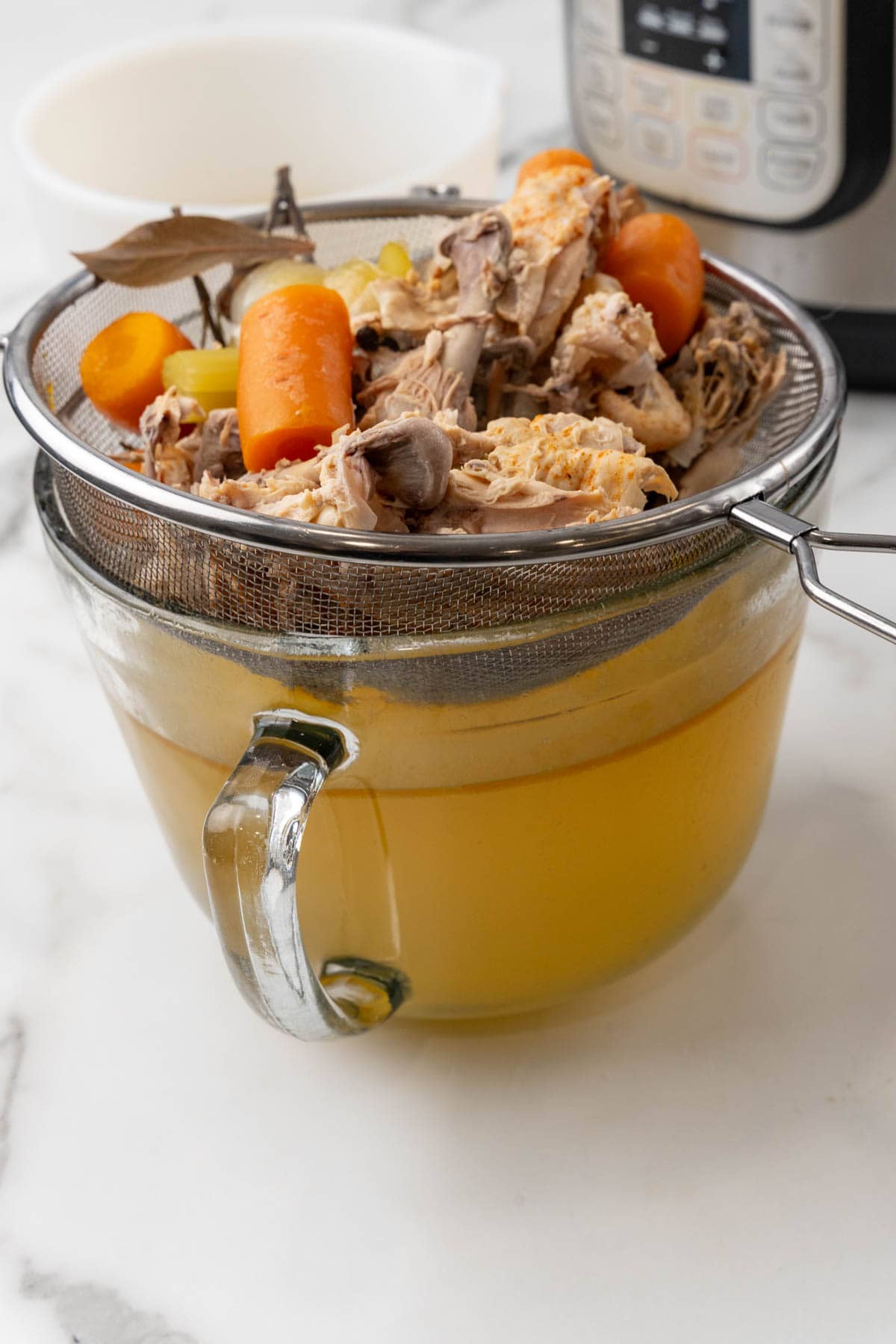 Chicken bone broth being strained into a glass bowl