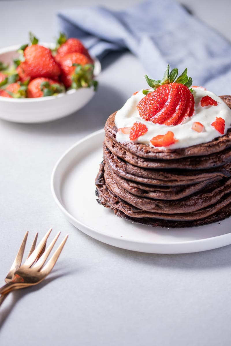 A stack of chocolate protein pancakes topped with whipped cream and a sliced strawberry