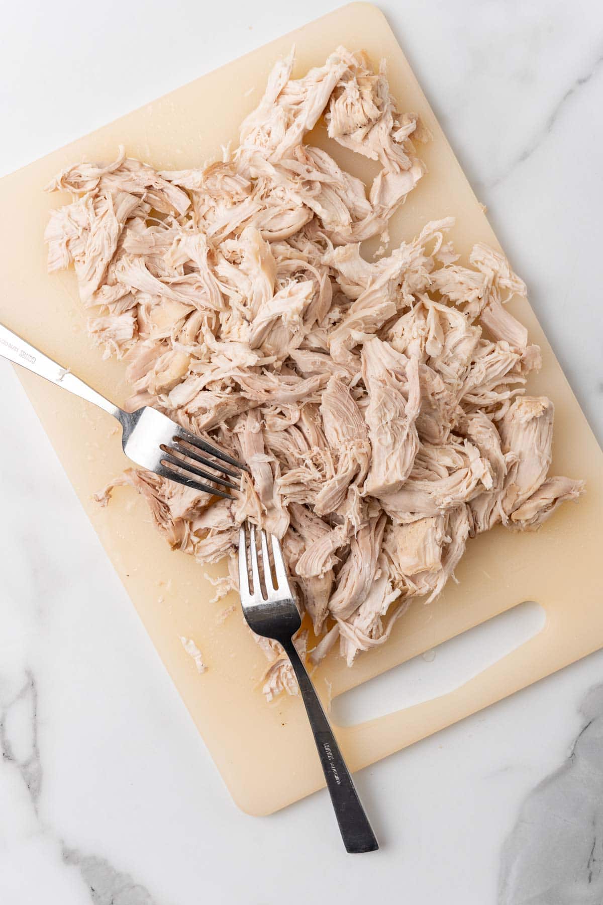 Shredded chicken breast on a cutting bord with two forks 