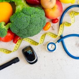 Healthy foods, a glucose meter and lancing device, a stethoscope and a measuring tape on a table