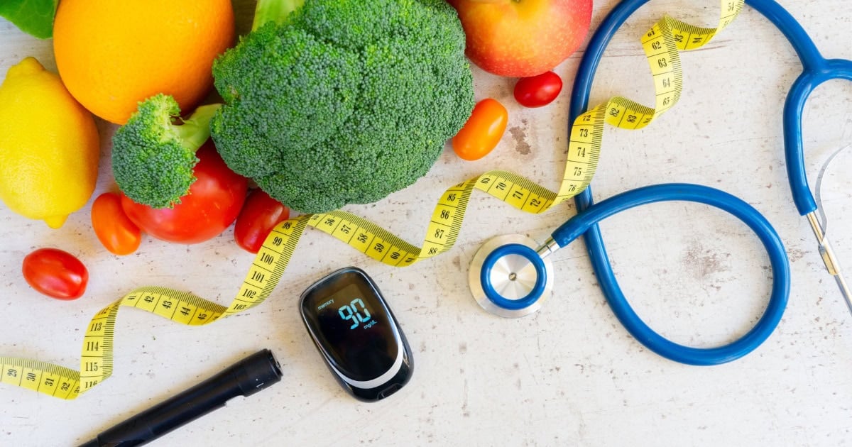 Healthy foods, a glucose meter and lancing device, a stethoscope and a measuring tape on a table