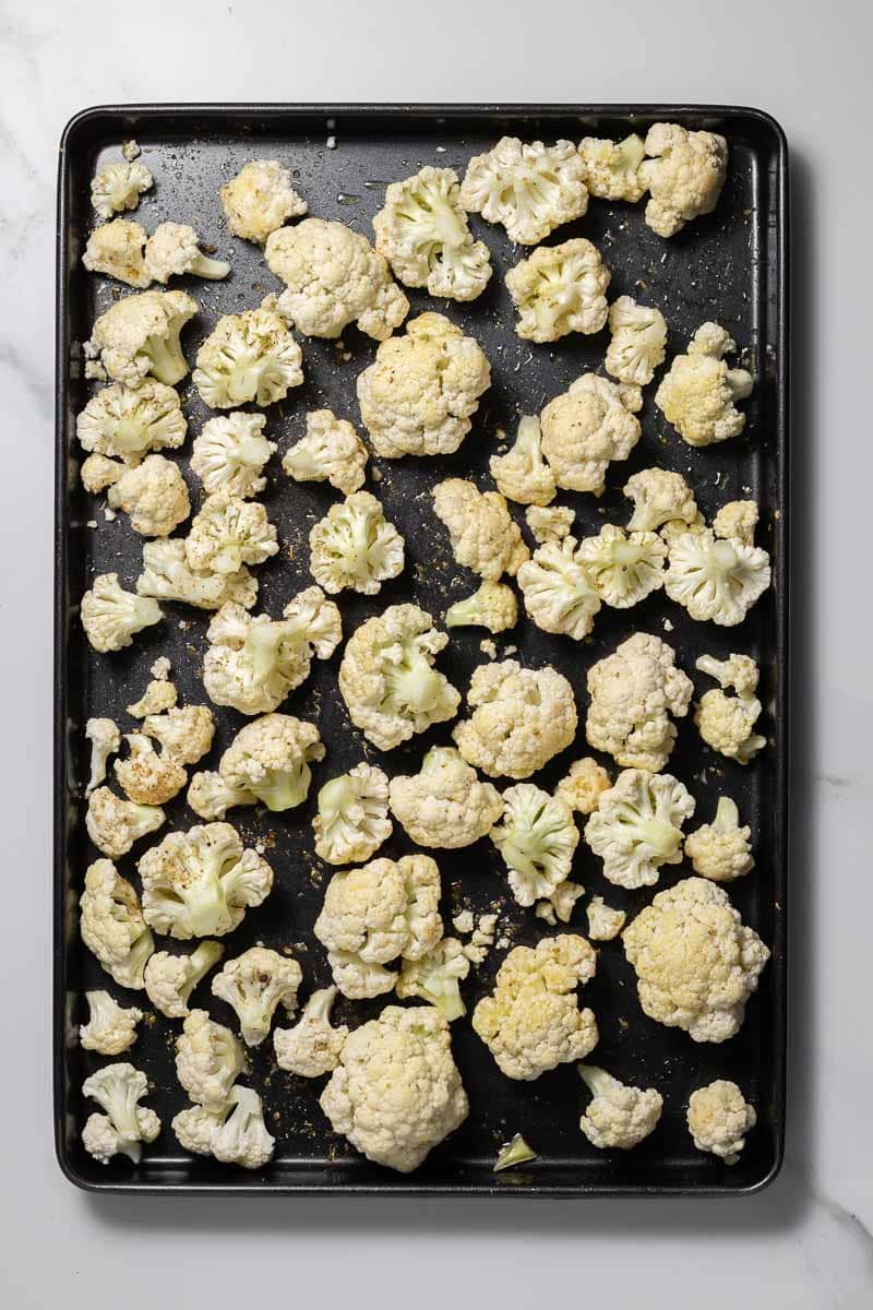 Raw cauliflower florets on a baking tray coated with olive oil and herbs 