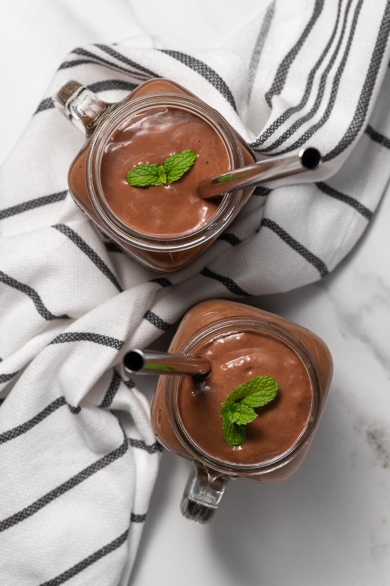 Chocolate avocado smoothie divided into two glasses and garnished with mint, as seen from above