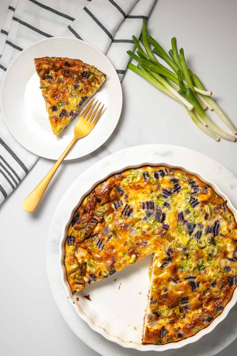 Low carb quiche in baking pan with one slice removed to a plate with a fork