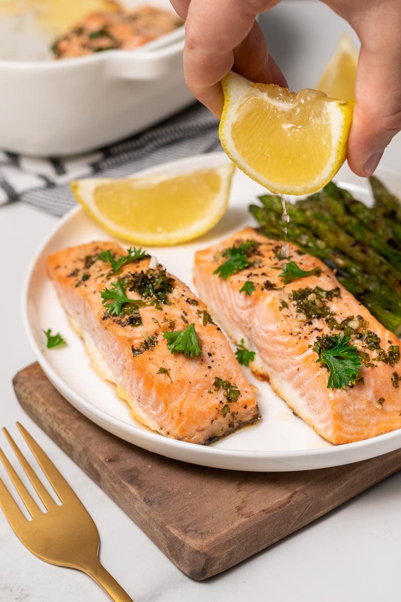 Baked Salmon on a plate with asparagus being drizzled with lemon juice